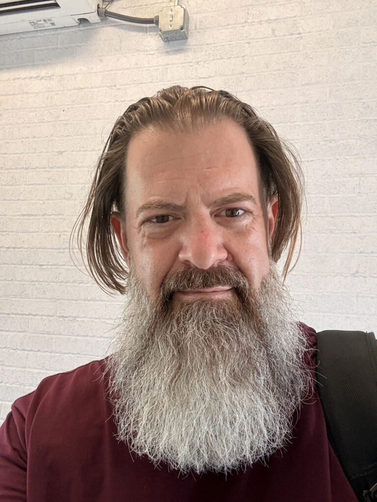 Loren Weisman in front of a white brick wall, August 12, 2026