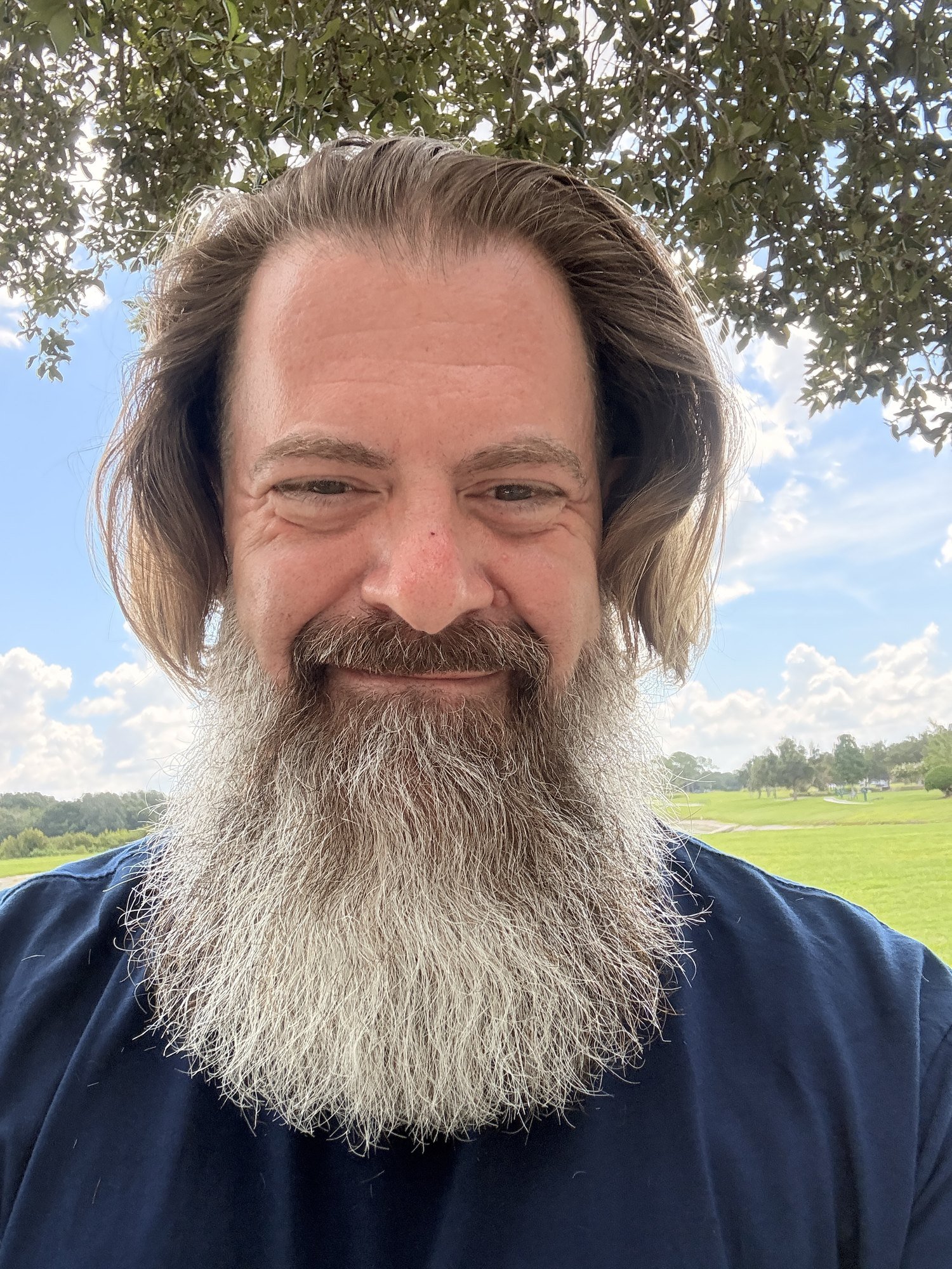 Loren Weisman, brand communications and optics strategist, outdoors in Florida under a tree with an open green field behind him