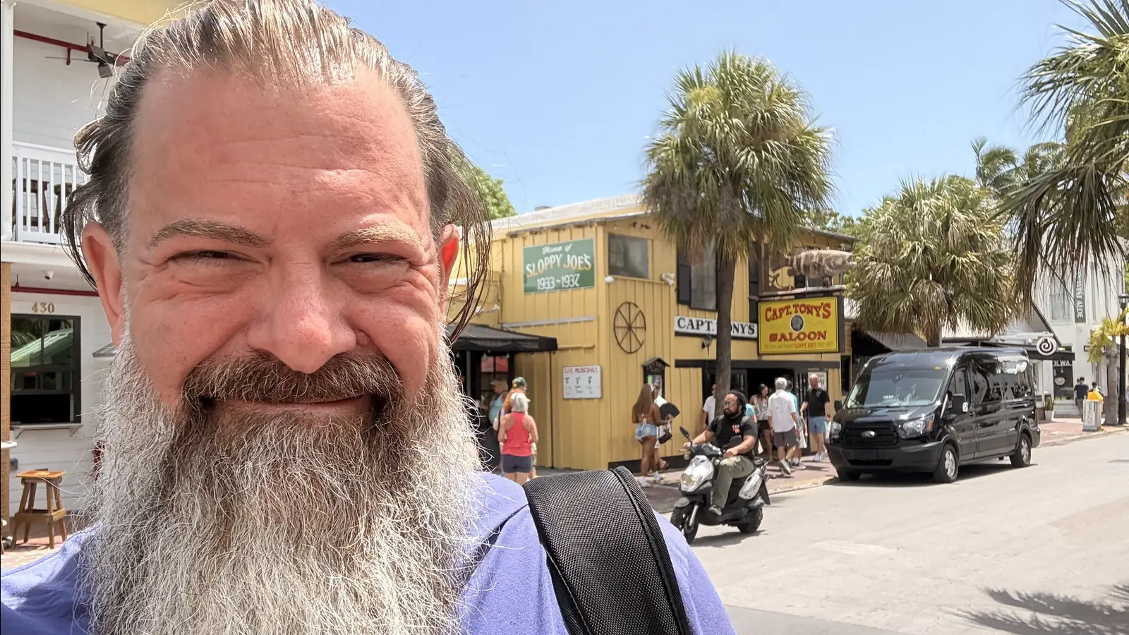 Loren Weisman on a Key West street, smiling, with shops, palm trees and passers by behind him.