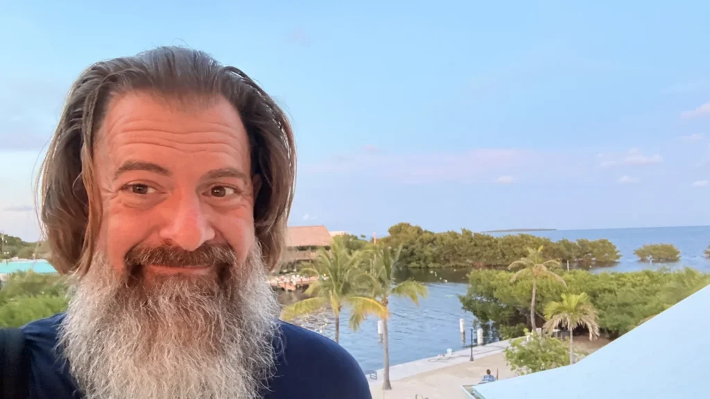 Loren Weisman at a Florida waterfront, smiling, with palms and open water behind him.