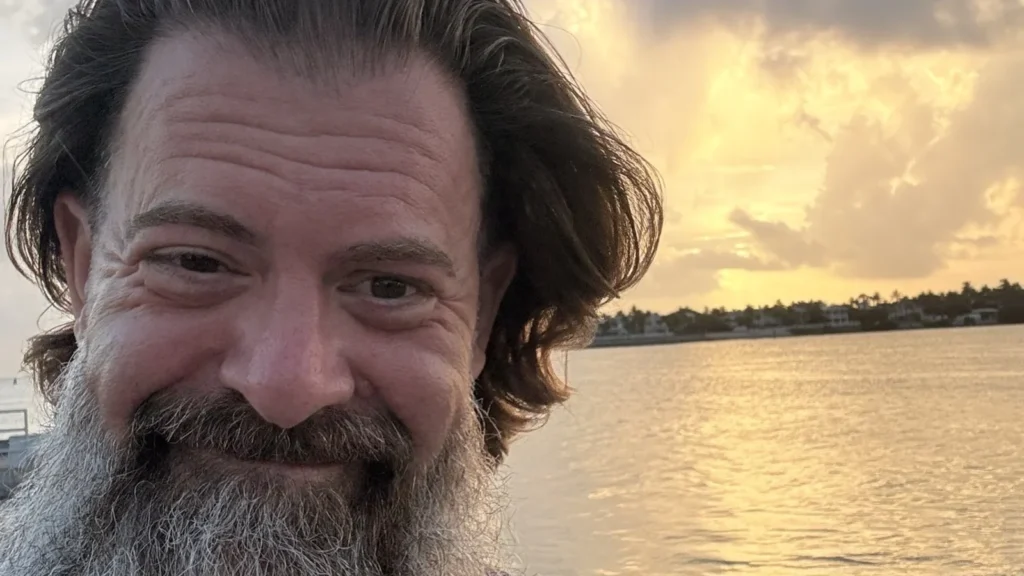 Loren Weisman, host of the Wait What Really OK podcast, at a waterfront at sunset.